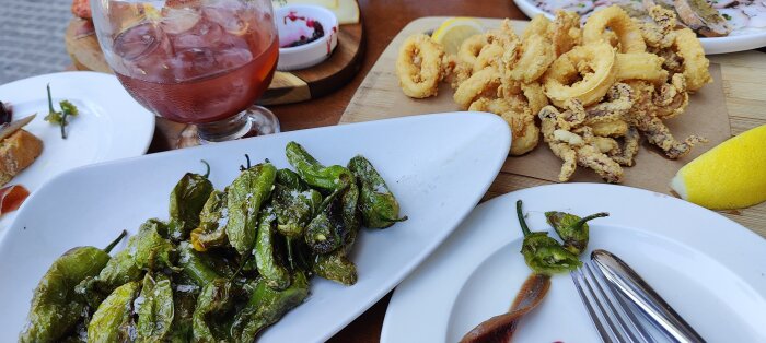 Friterade pimientos de padrón, bläckfiskringar, skivor av bröd och en rosa cocktail på uteservering.