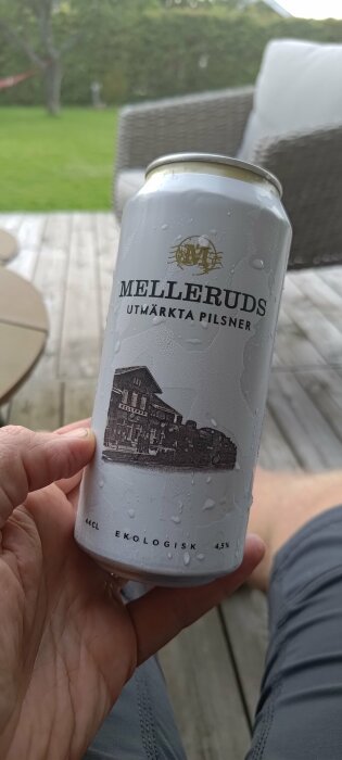 Person håller en ölburk märkt "Melleruds Utmarkta Pilsner", ekologisk, utomhusdag.