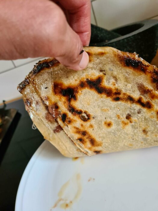 En hand håller en vikt quesadilla med stekytor, på en vit tallrik.