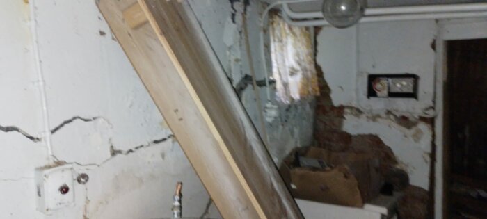 Förfallen interiör, skadade väggar, exponerat tegel, rörledningar, bråte, övergivet utrymme, renoveringsbehov.
