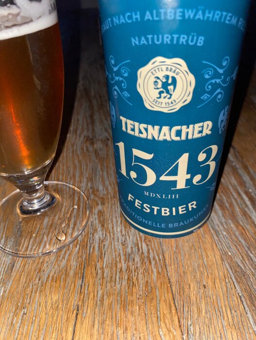 Ölglas med skum på träbord bredvid Teisnacher 1543 Festbier-flaska. Naturlig och traditionell bryggstil.