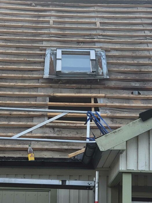 Renovering pågår, avtäckt tak med takfönster, stegar, byggmaterial synligt, temporär stödkonstruktion, ingen person, dagsljus.