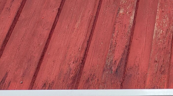 Rödmålat trä, vertikala plankor, slitet, textur, en vit del i bildens nederkant.