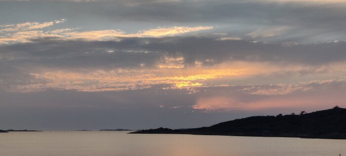 Solnedgång över havet, dramatisk himmel, moln, skymningsljus, silhuett av kustlinje.