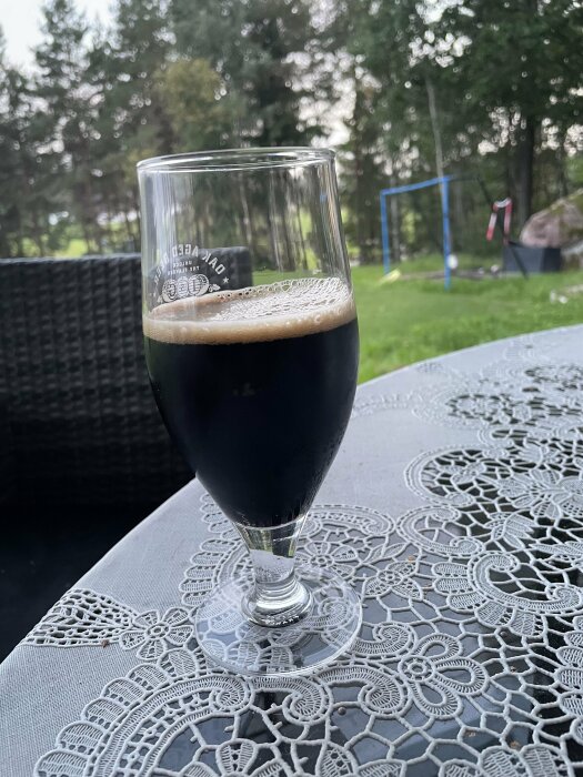 Öl i glas på spetsduk, utemöbler, trädgård med gräsmatta och lekställning i bakgrunden.