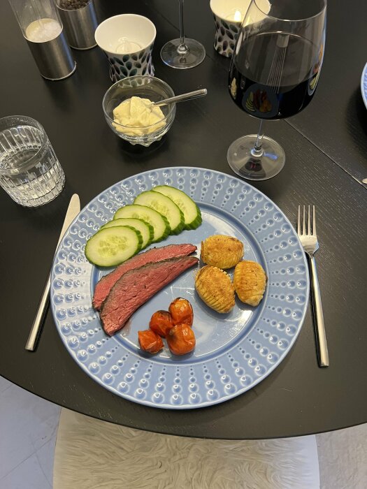 Måltid med kött, potatisgratänger, tomat, gurka, sås. Blå tallrik, dryck, modern design, bordsdukning.