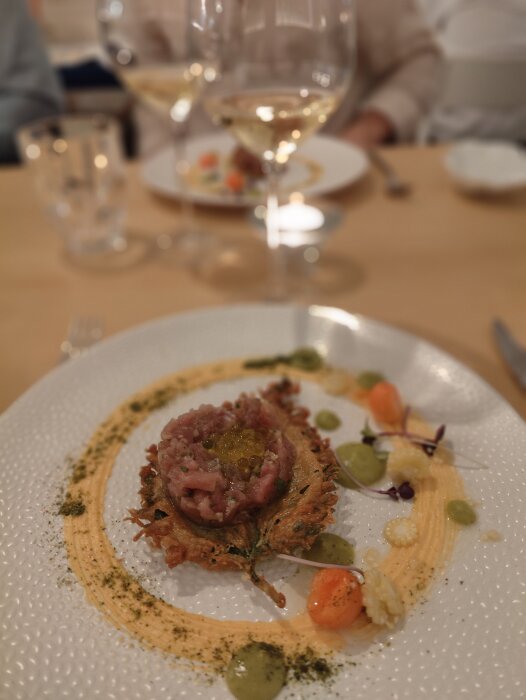 Elegant middagstillfälle, finmatig uppläggning av råbiff, vitt vin i glas, sofistikerad atmosfär.