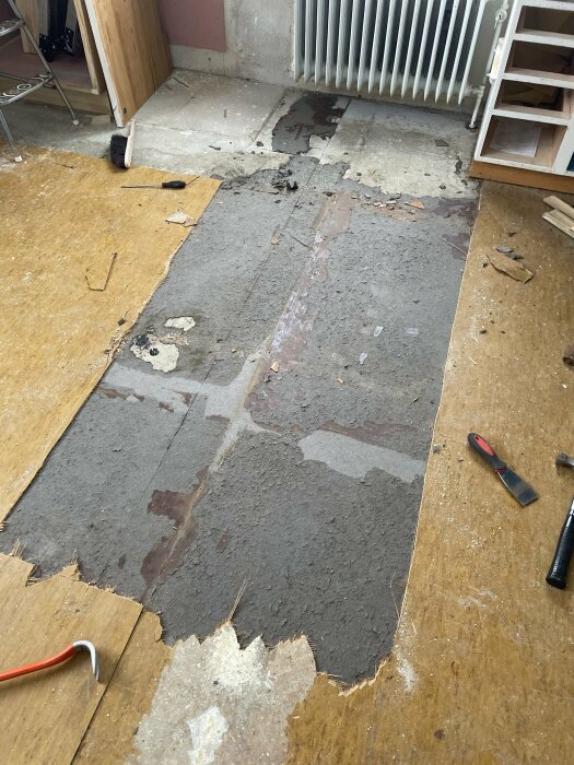 Renoveringsarbete på golv med synlig betong, verktyg, skräp och rivna delar av ytskikt.