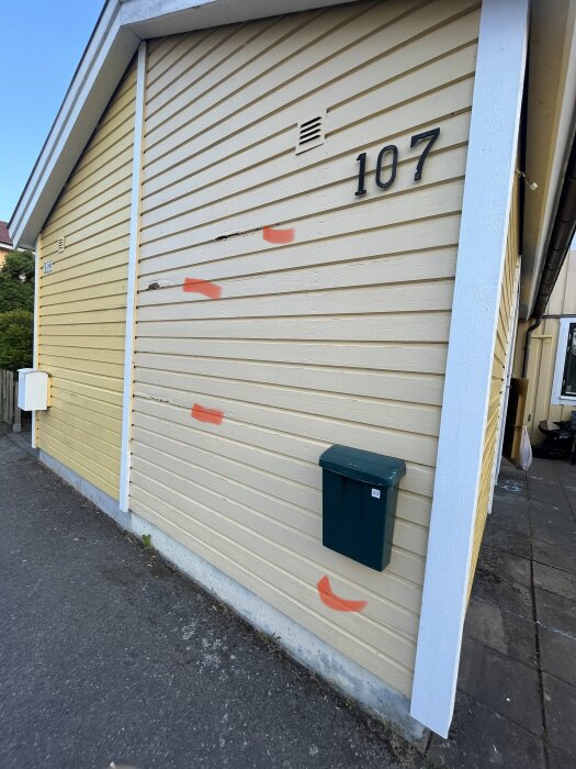 Beige garageport märkt "107" med röda sprayade pilmarkeringar och en grön brevlåda.