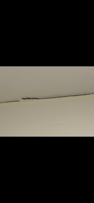 Lång spricka i en ljus yta, troligen på en vägg eller i ett tak. Strukturskada eller materialfel syns.