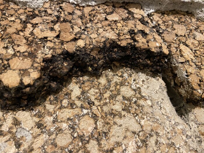 Närbild av sprucken, ojämn yta med bruna och svarta toner, möjligen asfalt eller gammal betong.