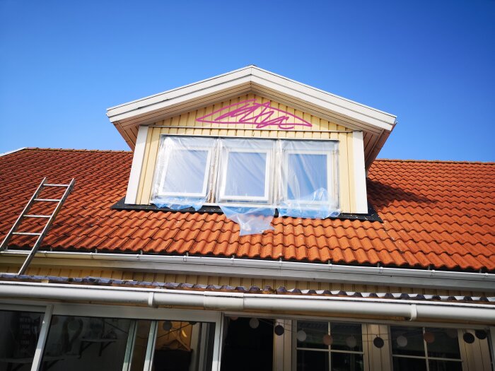 Gavel på hus med rött tegeltak, öppet fönster, plast, stege, blå himmel.