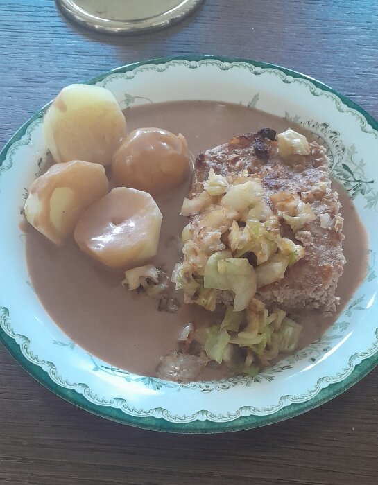 Ett måltid med potatis, brunsås, stekt kött och kokt vitkål på ett grönmönstrat porslinstallrik.