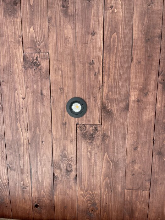 Träpanelvägg med en inbyggd rund taklampa mot en brun bakgrund.