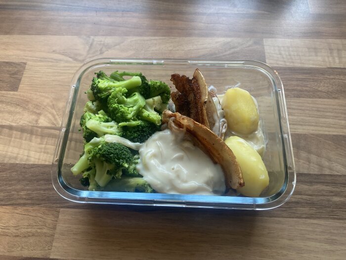 Matlåda med broccoli, kött, potatis och sås på träbord. Hälsosam, hemlagad mat.