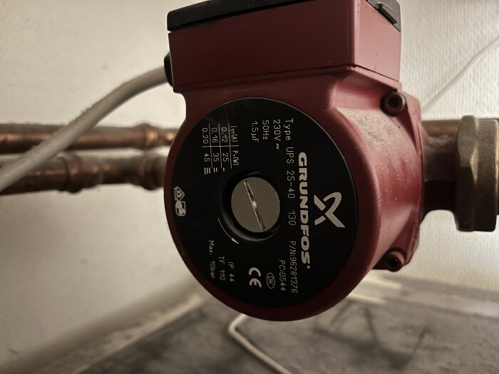 Grundfos cirkulationspump monterad på kopparledningar med inställningsratten i fokus.
