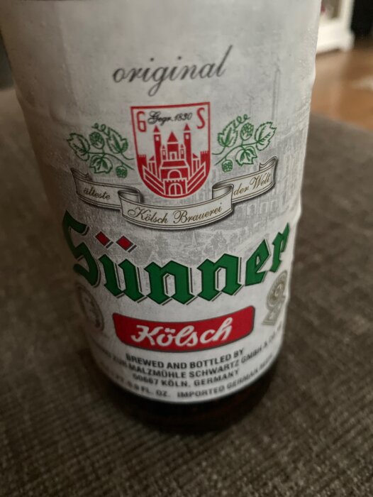 Ölflaska märkt "Sünner Kölsch", traditionell etikett, tyskt ölmärke, bakgrund otydlig, stående orientering.