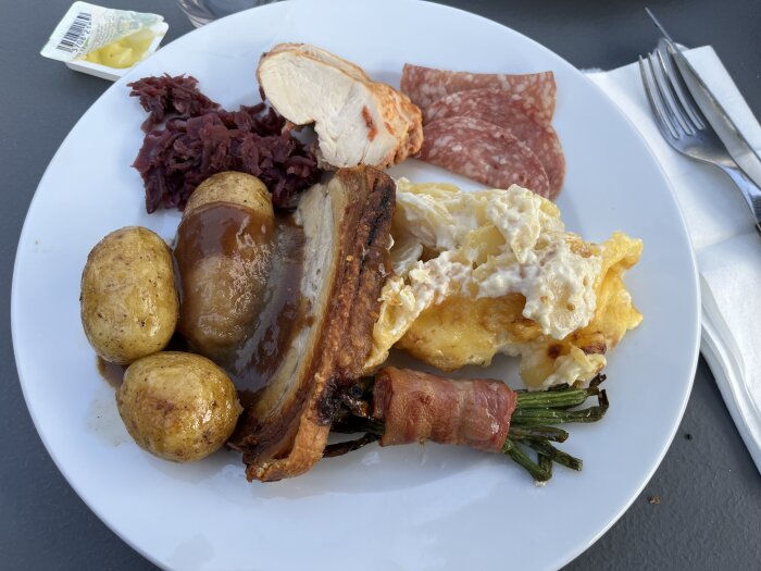 Ett tallrik med blandad mat inklusive kött, potatis, surkål, och fläsk i sås.