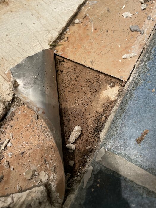 Öppet golv med brutna plattor och rester, visar underliggande material och möjlig byggarbetsplats.