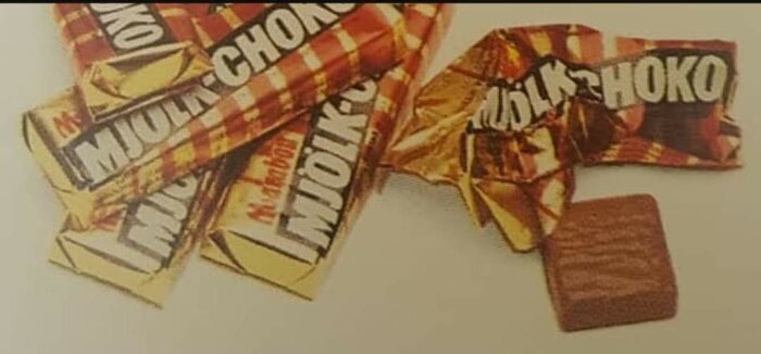 Flera oöppnade och öppnade chokladkakor med en synlig bit av chokladen. Rutmönstrat förpackningspapper.