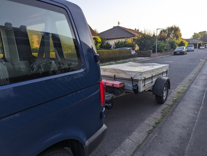 Blå skåpbil kopplad till en släpvagn parkerad längs en bostadsgata vid solnedgång.