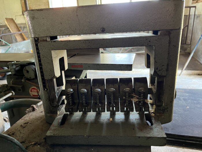 En gammal, smutsig verktygsmaskin med fjädrar och justerbara delar i en verkstadsliknande miljö.