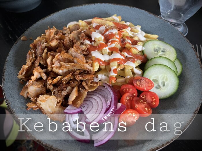 Tallrik med kebab, pommes frites, sås, tomater, gurka, lök, "Kebabens dag" text.