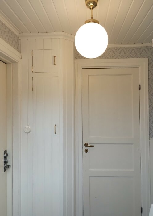 Inomhusmiljö, vit dörr, vita träpanelväggar, taklampa tänt, dekorativ tapet, byggnadsdetaljer, gammaldags, enkel elegant stil.