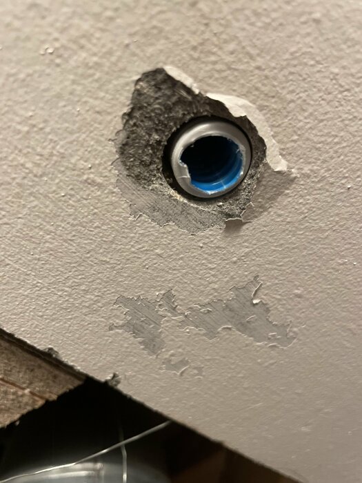 Ett hål i en grå vägg avslöjar en blå rördel inuti strukturen.