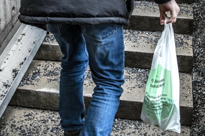 Person går i trappor med plastpåse, bär jeans och mörk jacka.