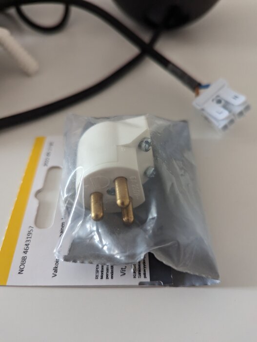 Förpackad elkontakt, glasögon i förgrunden, oskarp, kupplingsplint syns diffust.