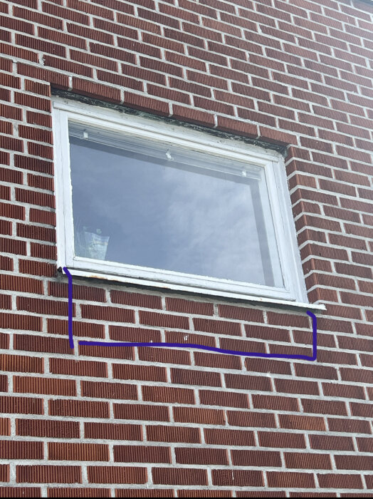 Ett vitfönster i en tegelvägg med blåa markeringar runt fönsterkarmens nedre del.