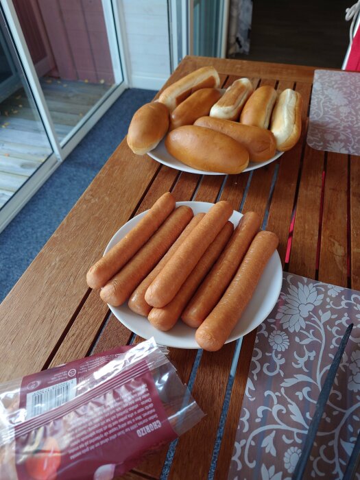 Träbord med korvar och korvbröd på tallrikar, förberedelse för måltid utomhus.