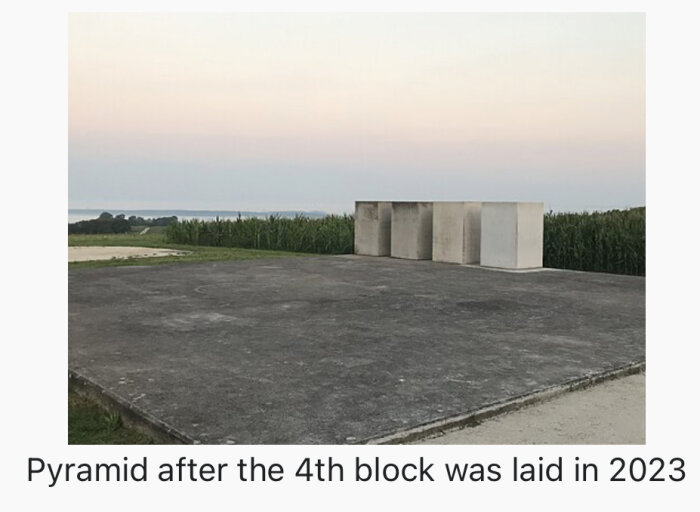 Betongblock utomhus, pyramidprojekt i början, skymning, åker i bakgrunden, 2023.