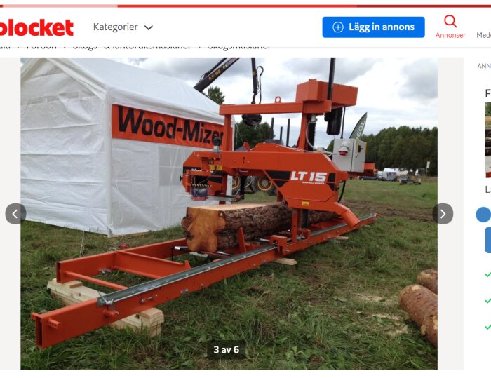 Orange bärbar sågverk utomhus, Wood-Mizer LT15, tält, trädstammar, gräsmark, molnig himmel.