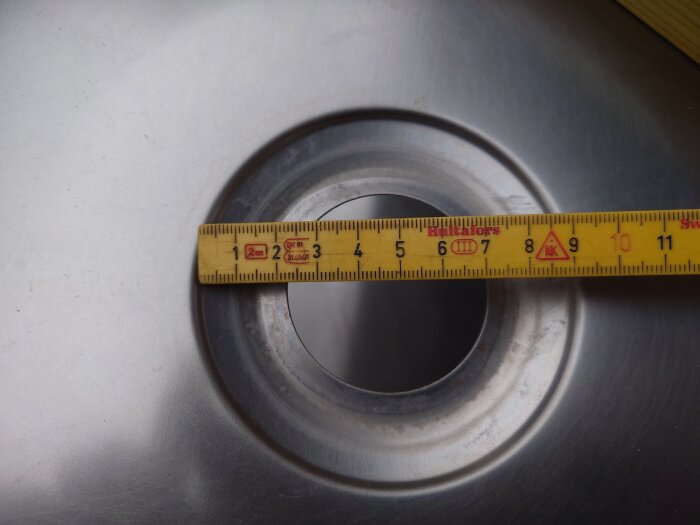 Ett måttband ligger över en rostfri diskho, visar cirka 11,5 centimeter.