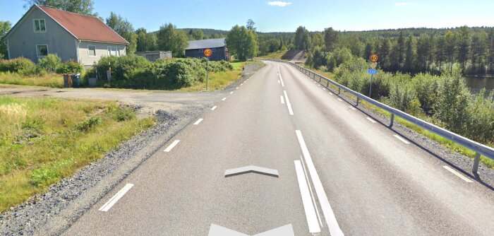 Lantlig väg, hastighetsskylt 60 km/h, sjö, gröna träd, soligt, hus, blå himmel, vägmarkeringar.