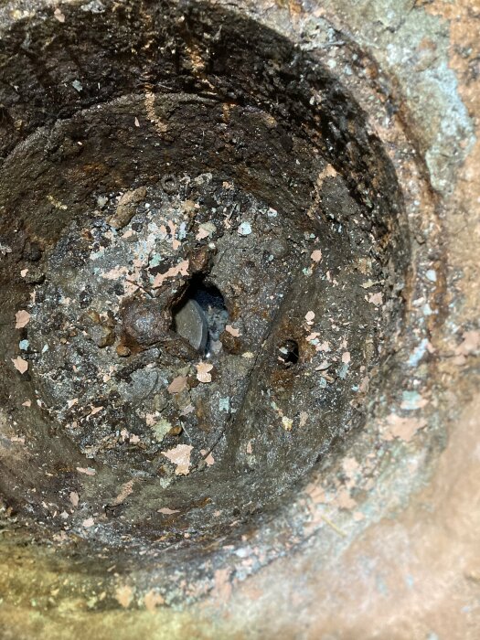 Rostig, degraderad metallyta med synligt slitage och förfall. Spår av korrosion och erosion inuti hålighet.