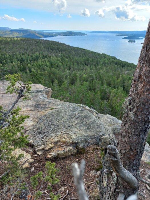 En utsikt från en klippkant över skog och en sjö med öar, molnig himmel, natur, friluftsliv.