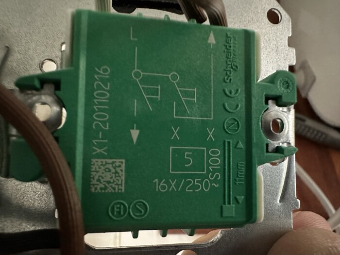 Grön Schneider Electric komponent, tekniska markeringar, QR-kod, säkringsliknande symboler, silverfärgad metall.