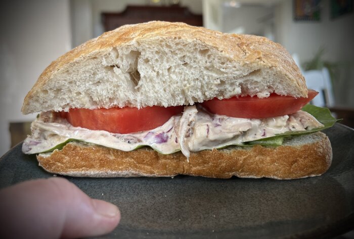 Ciabattabröd med kycklingröra, tomat och salladsblad på en mörk tallrik.