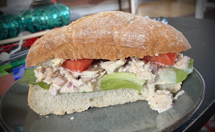 Halverat ciabattabröd med kycklingröra, sallad och tomatskivor på en tallrik. Fräsch, aptitretande, lunchtid.