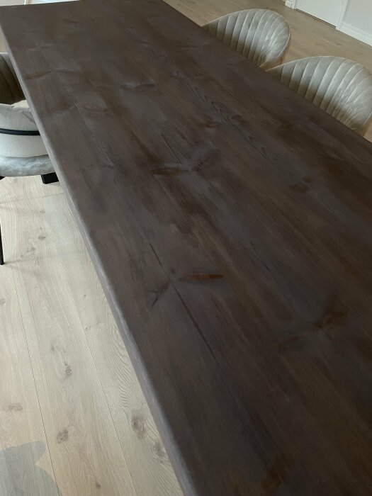 Mörkt träbord och två stoppade stolar på ett ljust trägolv i ett heminredningssammanhang.