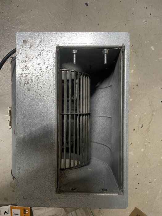 Industrifläkt eller ventilationssystem med visuell slitage, stålstångskydd, kablar, mot en betonggolvbakgrund.