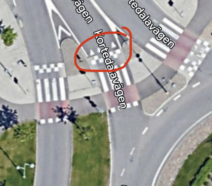 Flygbild på korsning med markerade vägbanor, övergångsställen, och röd cirkel runt vägskylttexten.
