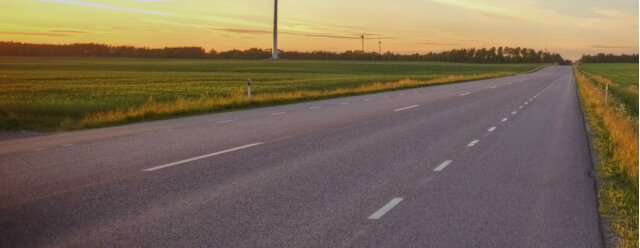 En väg som sträcker sig genom ett öppet fält vid solnedgång med mjuka färger och lugn atmosfär.