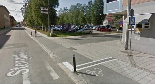 Gata med cykelbana, parkerade bilar, skyltar, byggnader, och en pollare vid övergångsstället.