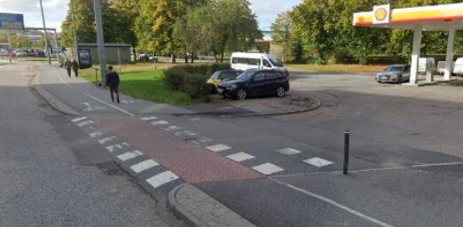 Bil körde upp på rondell, person går, mack i bakgrunden, dagtid, övergångsställe, stadsmiljö.