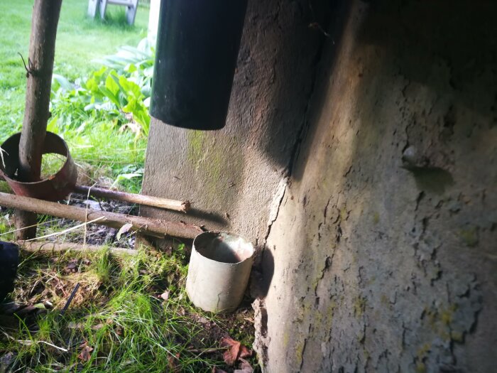 Rostiga verktyg lutar mot en vägg, växtlighet, en kruka och mossa, utomhus miljö.