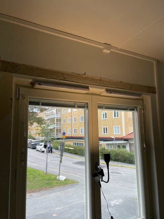 Ett fönster med utsikt mot en stadsgata, avskalat väggparti ovanför, delvis renoverat eller under konstruktion.